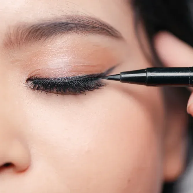 Close-up of woman applying water-based gel eyeliner above natural lash hairline with precision pen for defined look
