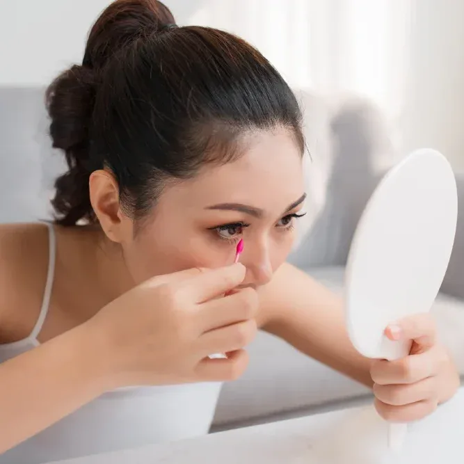Woman carefully applying dry powdery eyeshadow with finger while looking in mirror, creating dramatic eye makeup effect