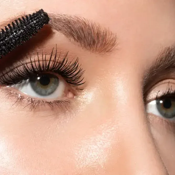 Woman applying mascara only to lower natural eyelashes with wand brush, enhancing eyes with careful makeup technique