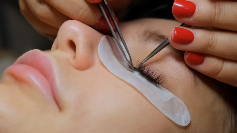 Professional beautician applies UV/LED eyelash extensions with precision tweezers on relaxed client