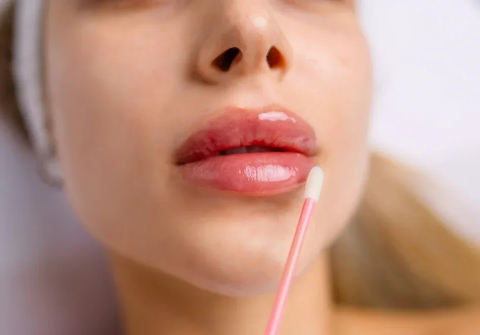 Client receives aftercare with cotton swab on swollen bright lips immediately after permanent makeup tattooing