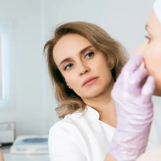 A client looks at her reflection while a dermatologist examines her skin, illustrating when to see a specialist for any skin concerns.
