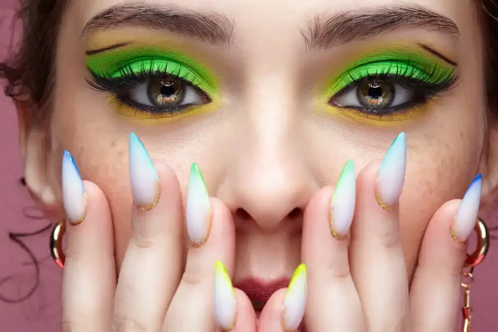 Woman wearing vibrant green lash extensions with bold eye makeup and colorful pointed nails, expressing 2025 trends