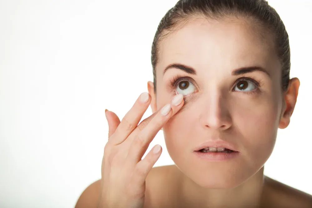 A woman inspects her eye with concern, representing the common myth that eyelash extensions ruin natural lashes.