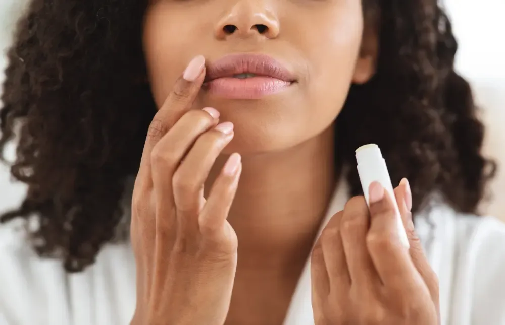 A close-up of a person applying an approved aftercare ointment from a tube to their lips, an essential step for proper lip blush healing.