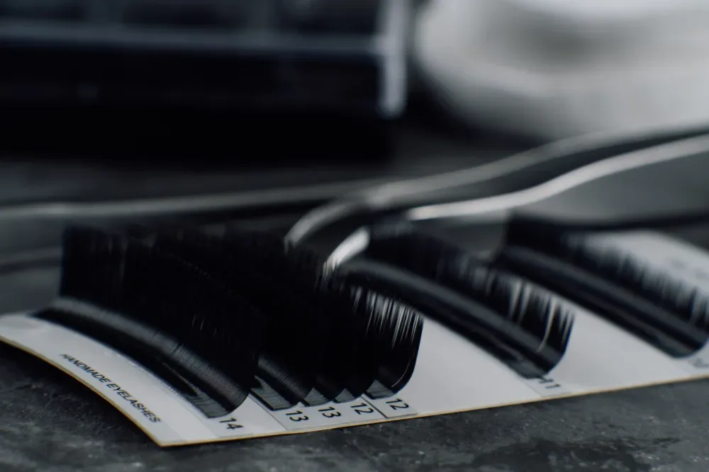 An artistic, black-and-white close-up of high-quality eyelash extension strips on a palette, representing professional-grade materials.