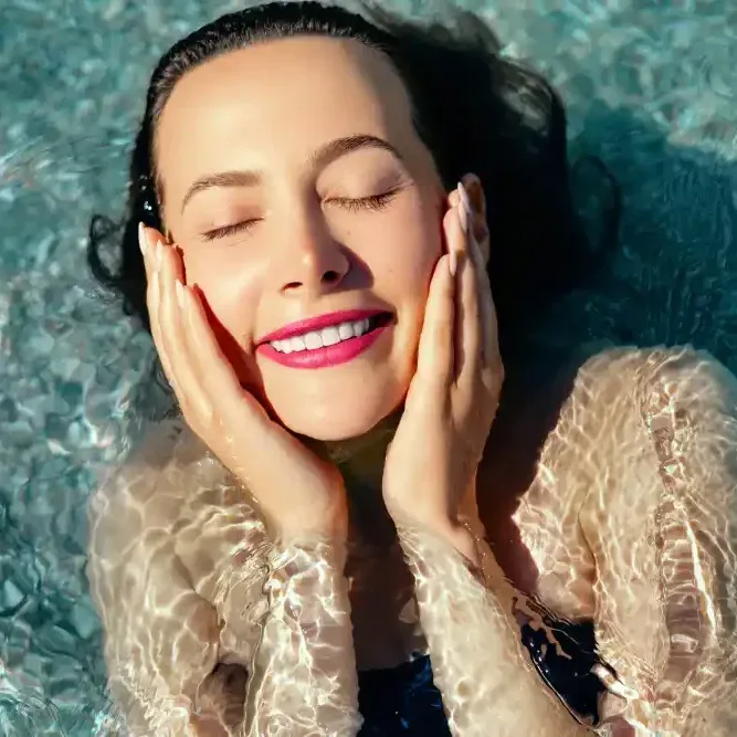 A woman with perfect, smudge-proof lipstick smiles while relaxing in the water, showcasing the long-lasting convenience and color of lip blushing.