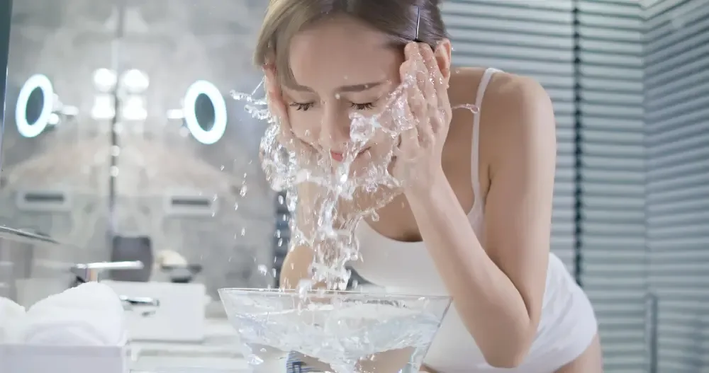A woman actively washes her face with water, demonstrating that you can and should get your lash extensions wet.
